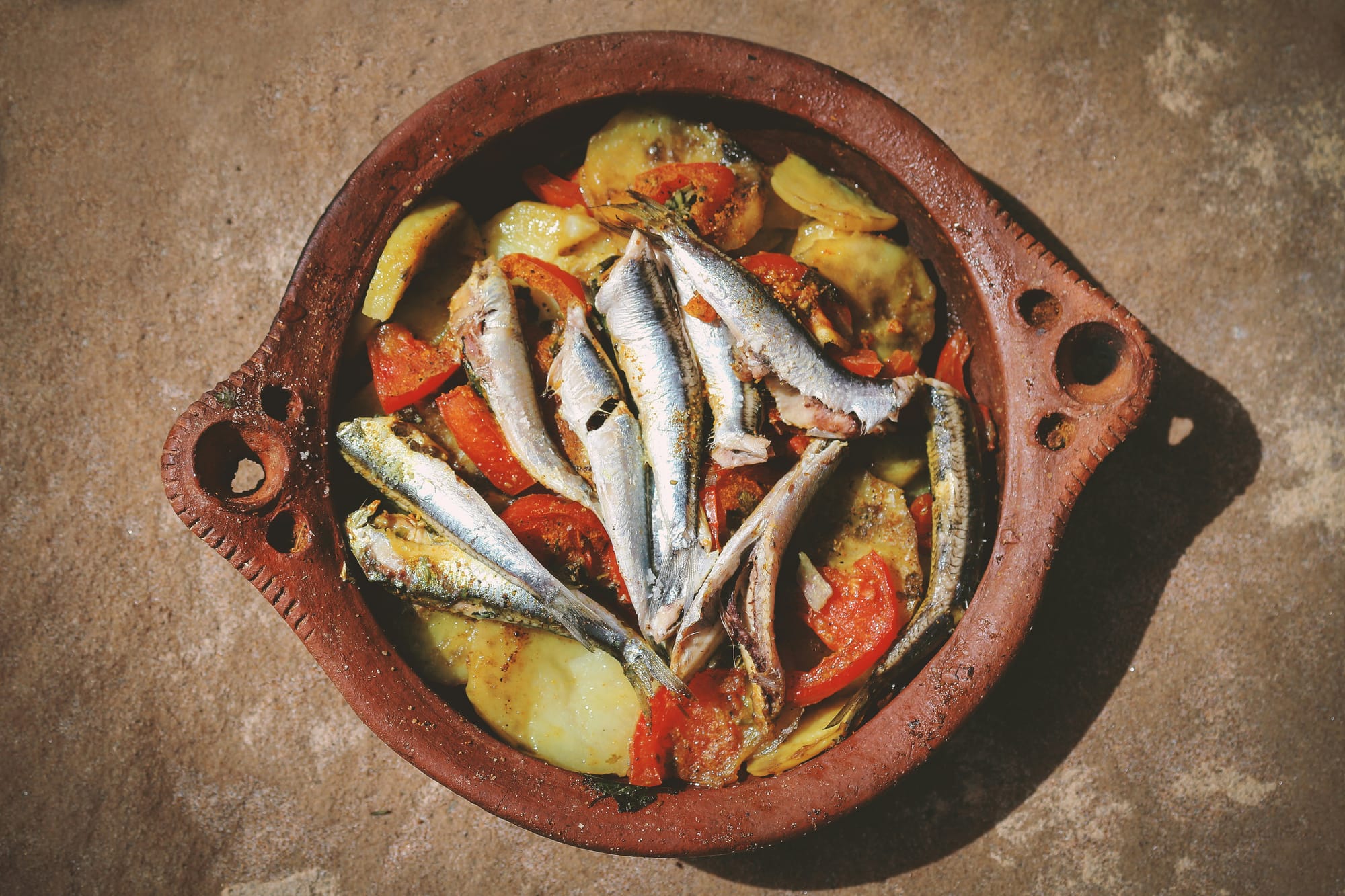 A photo of a dish filled with potatoes, fish and tomatoes.