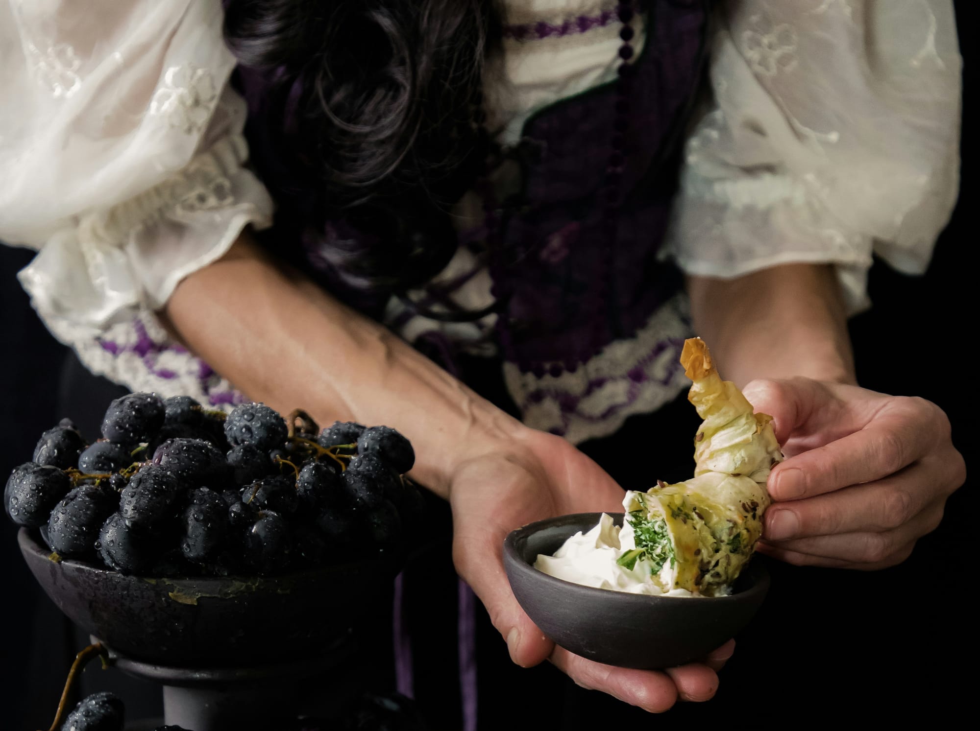 A photo of a person dipping a pastry into a bowl of cream.